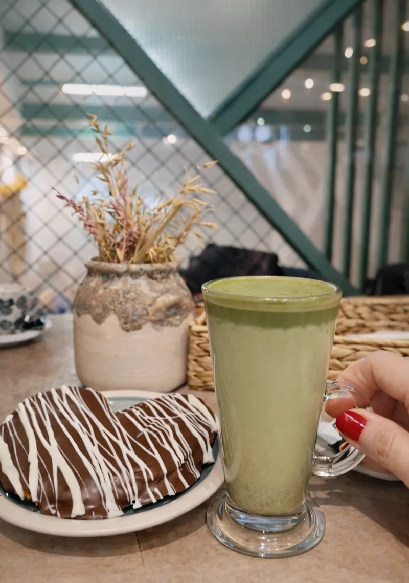 Bebida verde en vaso alto junto a una palmera de chocolate